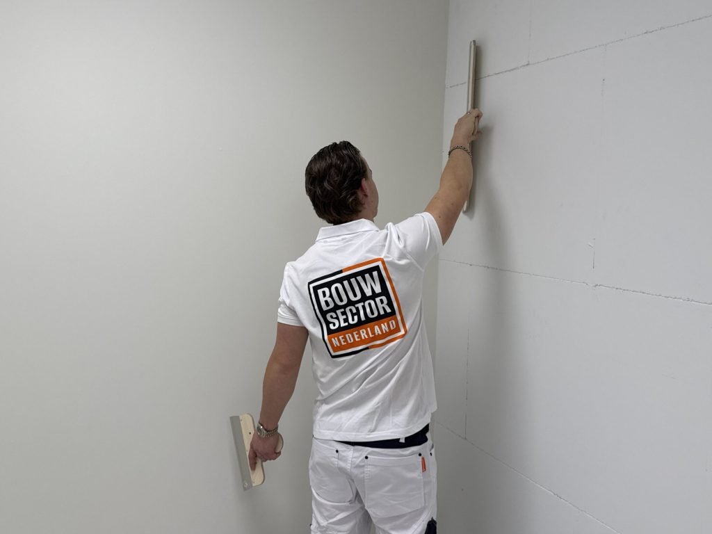 Stukadoor strekt zijn arm en zet een rei langs een wand in de hoek van een lege kamer