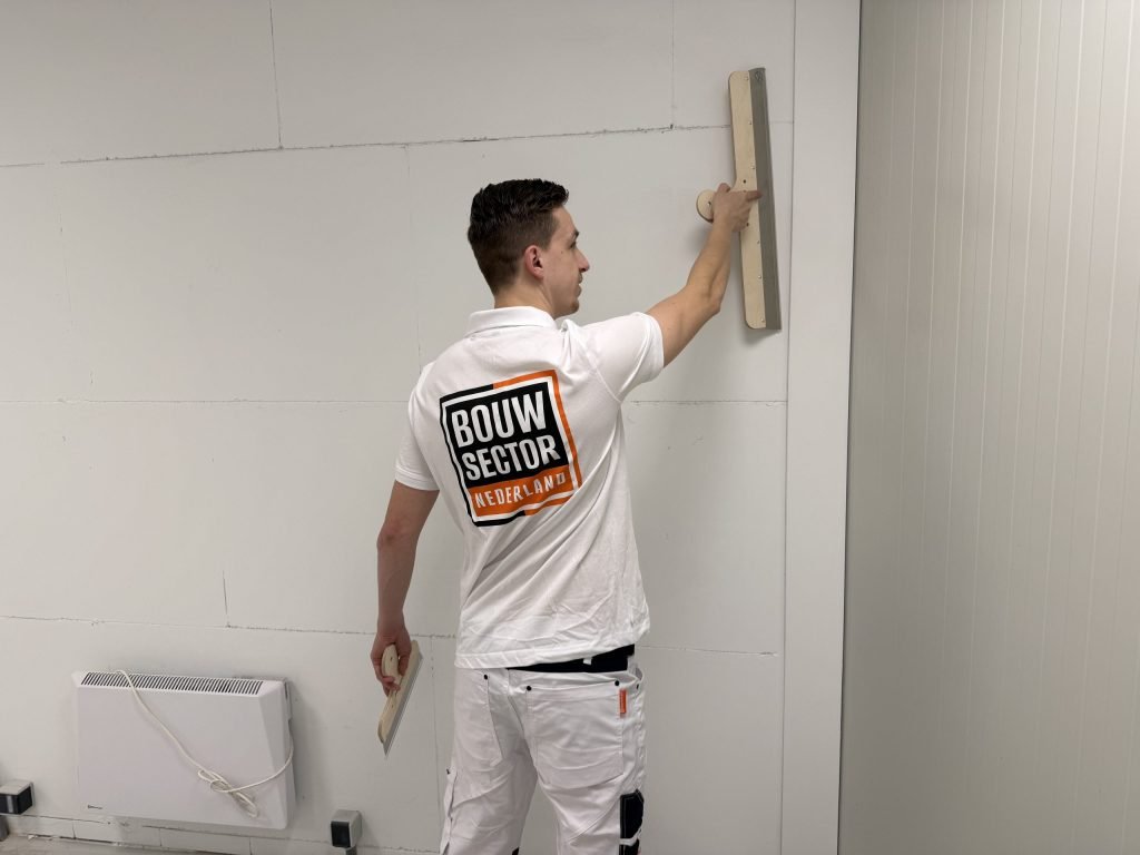 Stukadoor met het logo van Bouwsector Nederland op zijn rug trekt een wand boven een elektrische kachel vlak