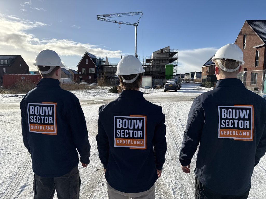 Drie medewerkers van Bouwsector Nederland met witte helmen kijken naar bakstenen woningen in aanbouw